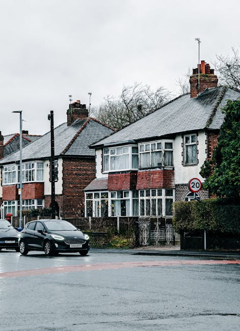 A row of traditional semi-detached houses with brick and white rendered facades, situated along a residential street. Each house features large bay windows with white frames, tiled roofs with chimneys